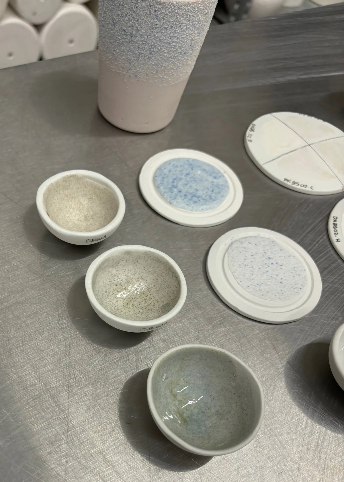Small ceramic glaze tests on a stainless-steel work surface